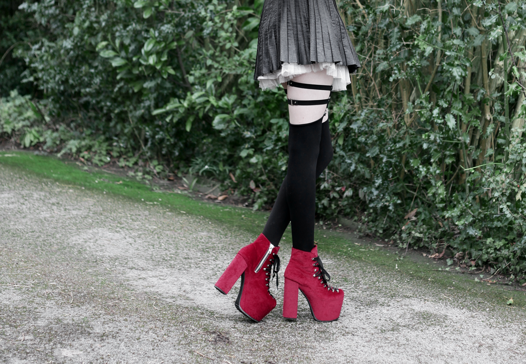 Olivia Emily wears Contrast Collar Black Blouse, Asos Western Belt, Pleated Faux Leather Skirt, Jakimac Leg Garter Harnesses, Unif Red Velvet Hellbound Boots
