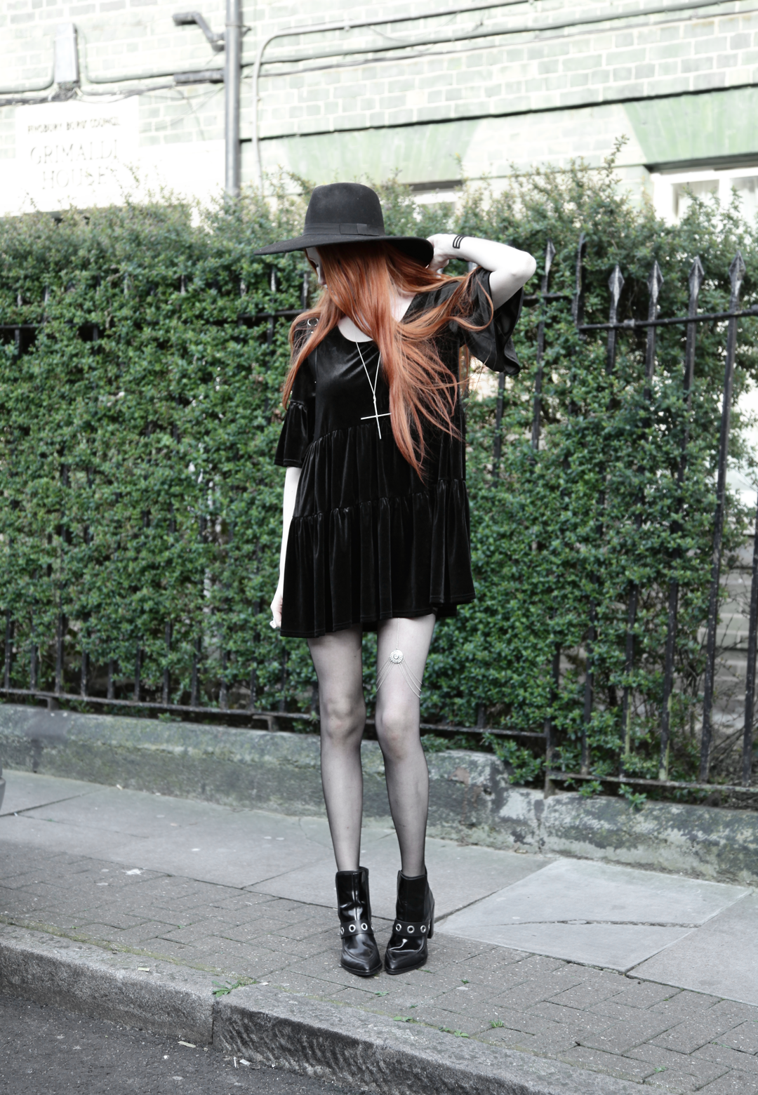 Olivia Emily wears Asos Reclaimed Vintage tiered black velvet dress, Killstar Witch Brim hat, River Island leg chain, and Asos eyelet boots