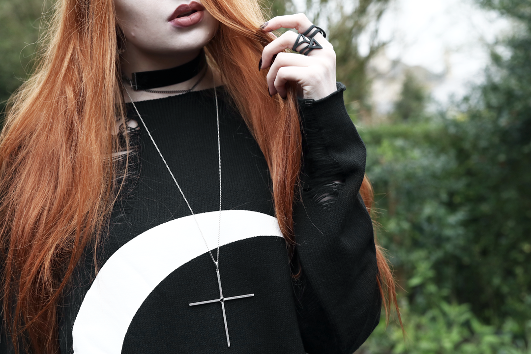 Olivia Emily wears Killstar oversized Luna moon sweater, Regalrose velvet choker, Killstar dagger earrings, The Rogue and The Wolf matte black rings and Kiki Minchin silver Classic Cross necklace