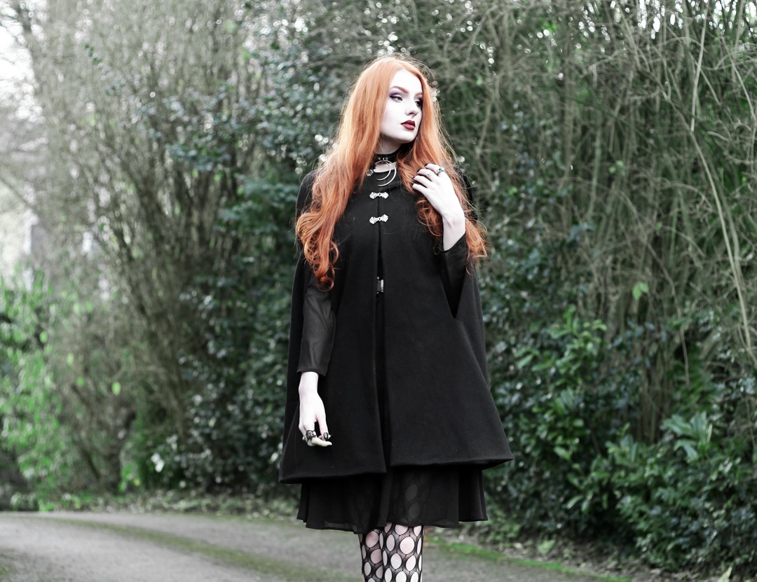 Olivia Emily wears Dark Thorn Clothing Myrtle Cape, Asos black ruffle midi dress, Killstar Dita Slave collar choker, and Asos pothole tights