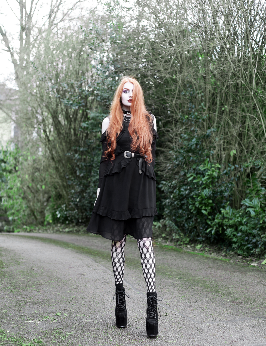 Olivia Emily wears Asos black ruffle midi dress, Killstar Dita Slave collar choker, Asos western belt, Asos pothole tights, and faux suede platform heels boots