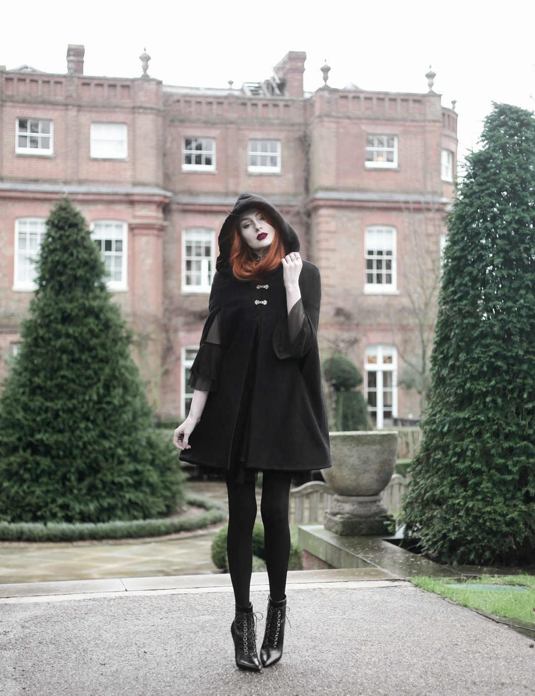 Olivia Emily wears Dark Thorn Clothing Cape, Killstar Nu Decay Dress, and Saint Laurent Fetish Ankle Boots