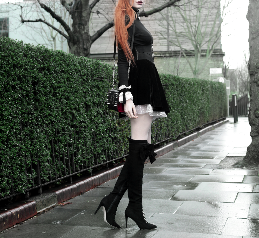 Olivia Emily wears Skinny Bags Dark Thoughts Clutch, River Island High Neck Top, Asos Ruffle Cuffs, Black Velvet Skirt, and Asos Lace Up Boots